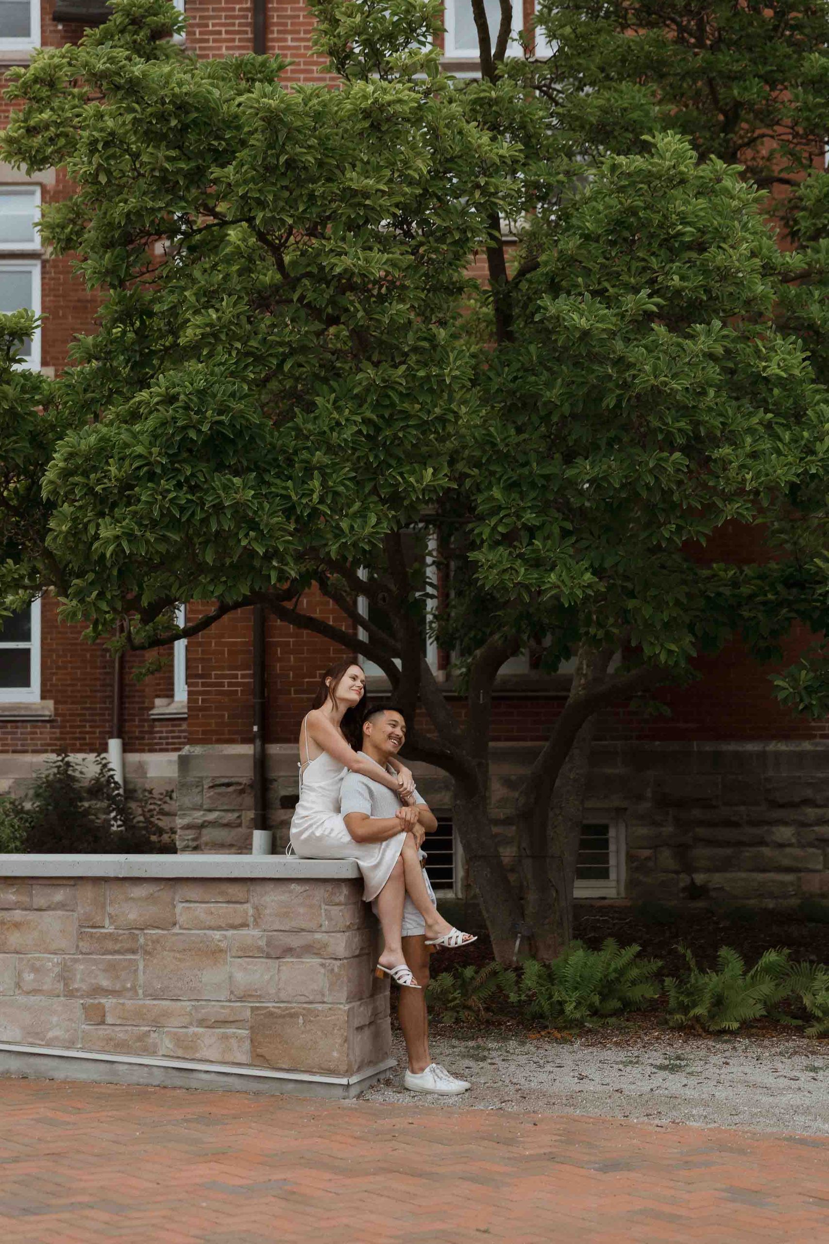 Engagement photos at Guelph University outside the old buildings | Sonia V Photography sitting on stone wall under tree