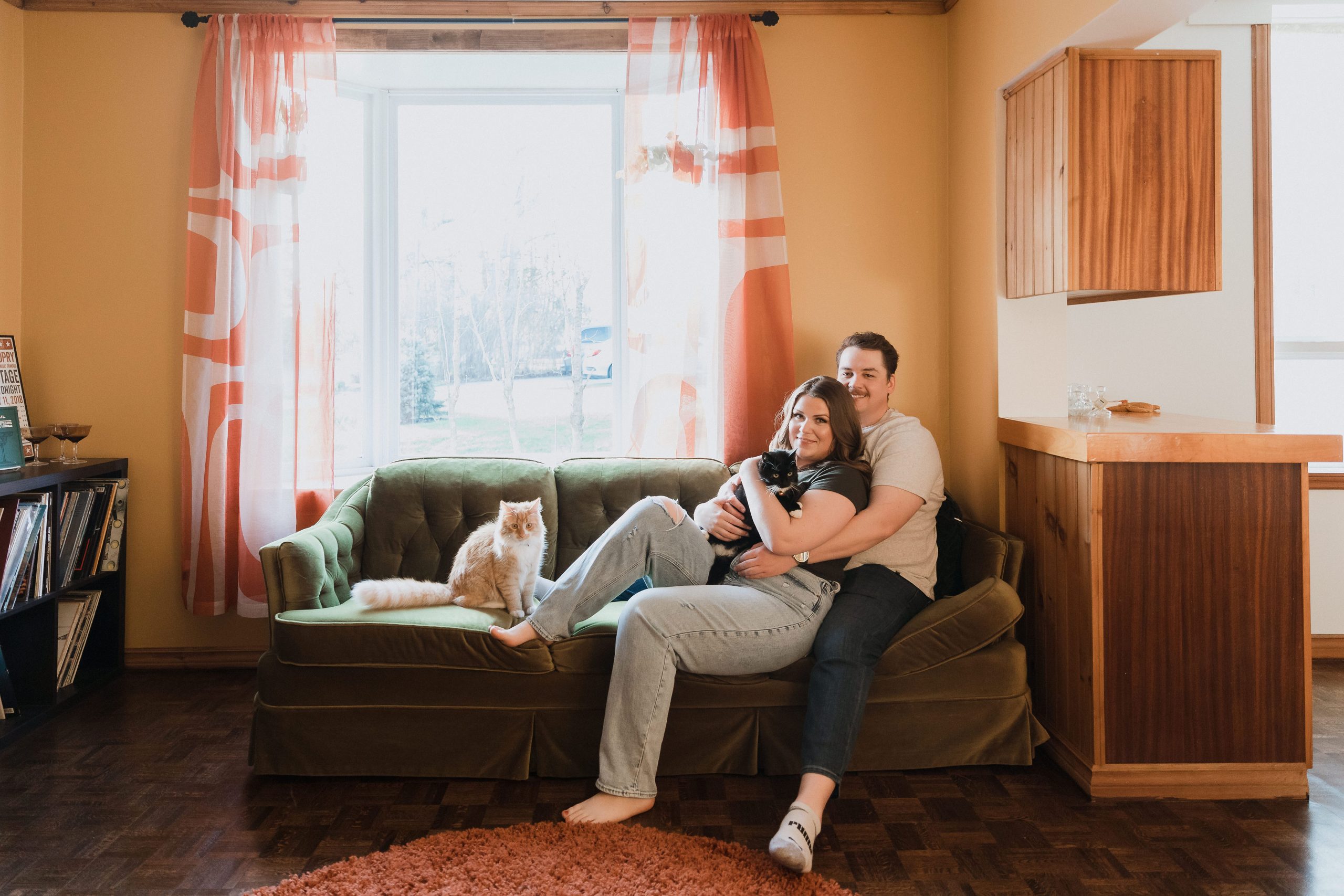 Couple sitting on the couch in orange living room retro style interiors in their home in rural Ontario, in-home engagement photos by Sonia V Photography