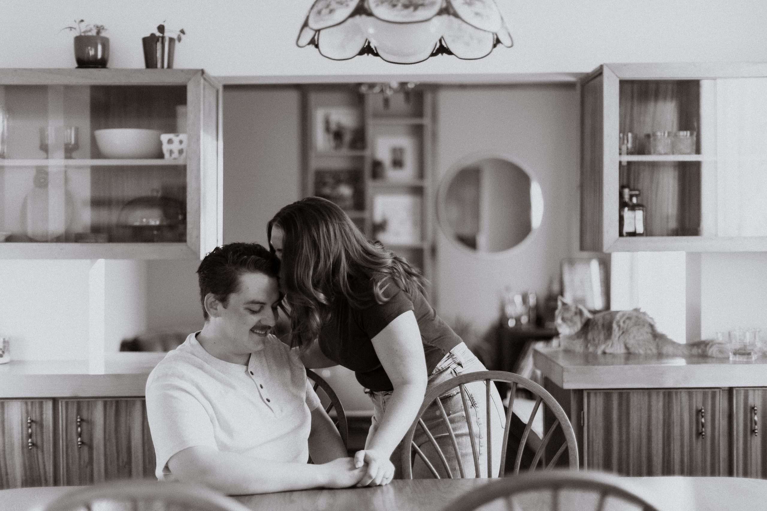 Couple sitting on the kitchen counter in orange living room retro style interiors in their home in rural Ontario, in-home engagement photos by Sonia V Photography
